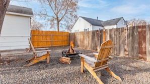 Ein Garten mit Feuerstelle, zwei Adirondack-Stühlen aus Holz und einem Holzzaun.