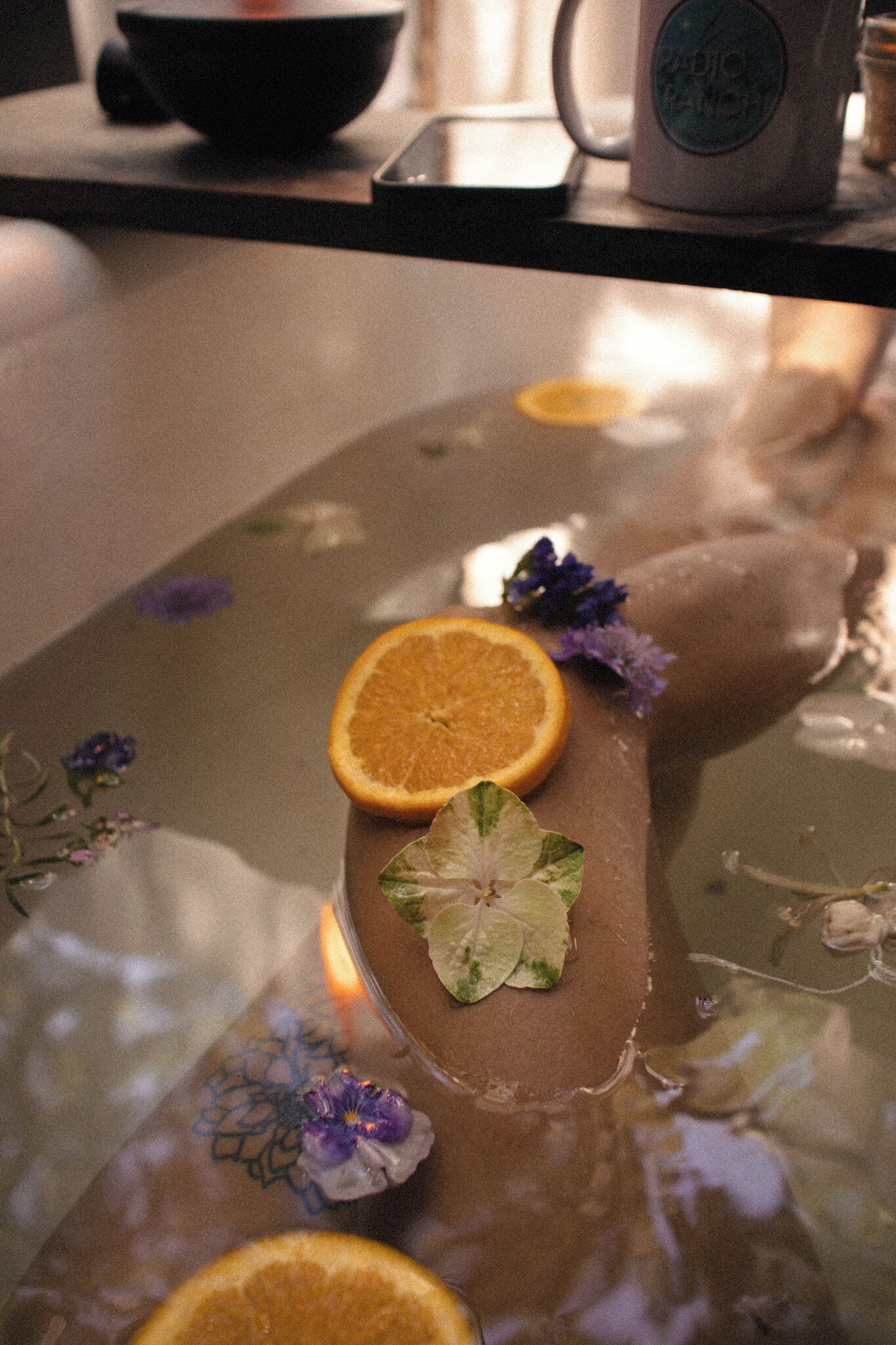 A dessert with orange slices and flowers on a reflective surface.