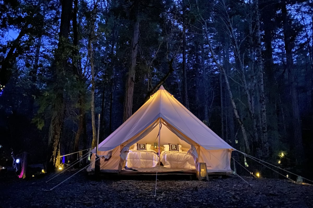 A tent with a triangular roof and a bed inside, surrounded by trees.