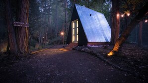 A cabin with a sloped roof, surrounded by trees, and a sign welcoming visitors to Alpine Camp. - Radio Ranch (Burnt Ranch)