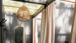 A small, enclosed space with a metal-framed ceiling, a wicker hanging light fixture, a mirror, striped curtains, a potted plant, and a basket labeled "TOWELS". - Radio Ranch (Burnt Ranch)