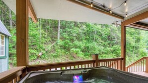 A hot tub with a waterfall feature, surrounded by a wooden deck and a forest view. - King Branch Rd · 3BR | Hot Tub | Dog Friendly | Wi-Fi | Games (Sevierville)