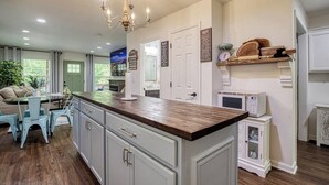 A kitchen with a central island, white cabinetry, and a chandelier. There are two doors, a microwave, and a small cabinet. - King Branch Rd · 3BR | Hot Tub | Dog Friendly | Wi-Fi | Games (Sevierville)