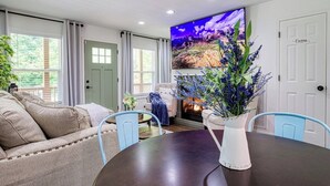 A living room with a fireplace, a sofa, a dining table, and a large TV mounted on the wall. - King Branch Rd · 3BR | Hot Tub | Dog Friendly | Wi-Fi | Games (Sevierville)
