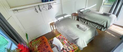 A room with two beds, a small table with a colorful tablecloth, and a shelf with a patterned cushion.
