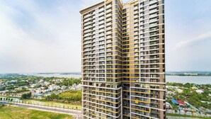 A high-rise building with multiple balconies and a view of a river and greenery in the background.