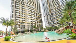 A modern high-rise residential building with a swimming pool surrounded by palm trees and rocks.