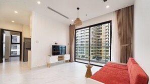 A modern living room with a red sofa, a TV on a white cabinet, and a large window with curtains.