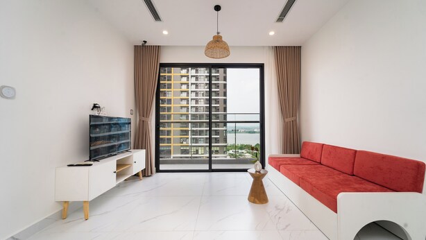 A modern living room with a red sofa, a white TV stand, and a large window with curtains.