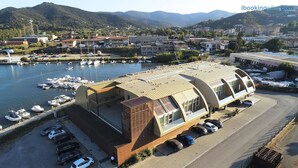 A modern building with a curved roof, parking area, and boats in the background. - Fronte Mare Suites - Fronte Mare Suites - Studio (H) (Portoferraio)