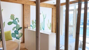 A room with a wooden ceiling, a cactus wall mural, a white desk, and a view of a pool through large windows. - Fronte Mare Suites - Fronte Mare Suites - Studio (H) (Portoferraio)