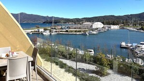 A view of a marina with boats docked, a mountainous backdrop, and a table with breakfast items on a balcony. - Fronte Mare Suites - Fronte Mare Suites - Studio (H) (Portoferraio)