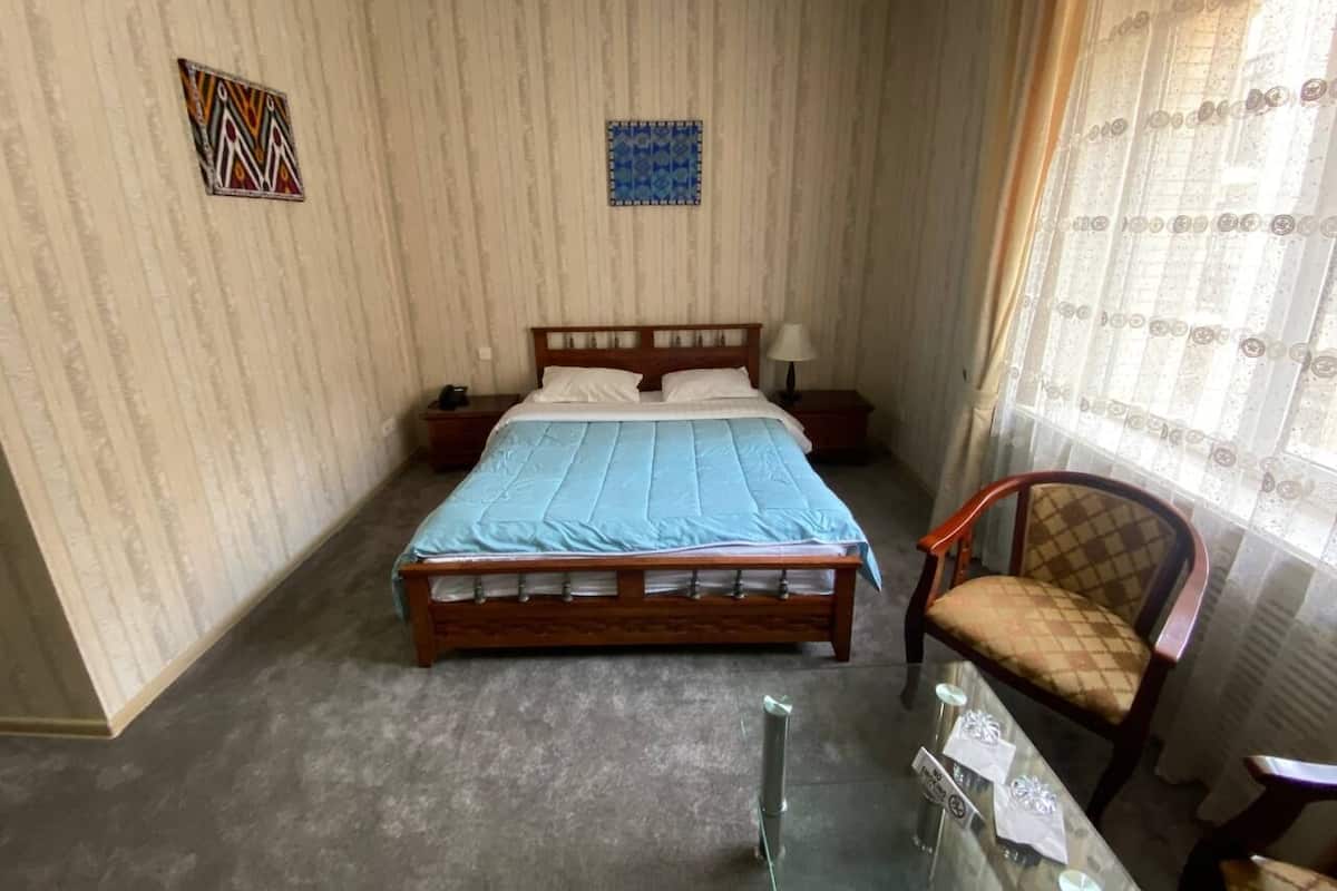 A bedroom with a large bed, a chair, a nightstand, and a small table.