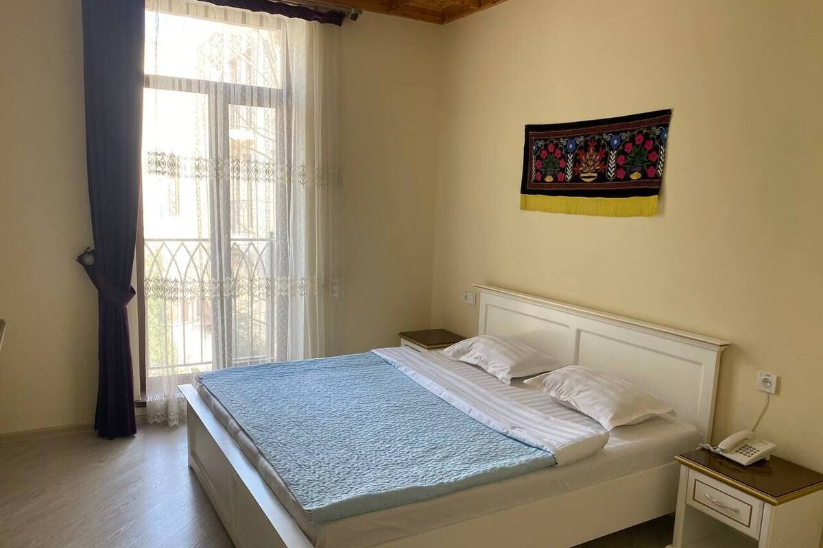 A bedroom with a bed, a nightstand, a telephone, and a window with curtains.