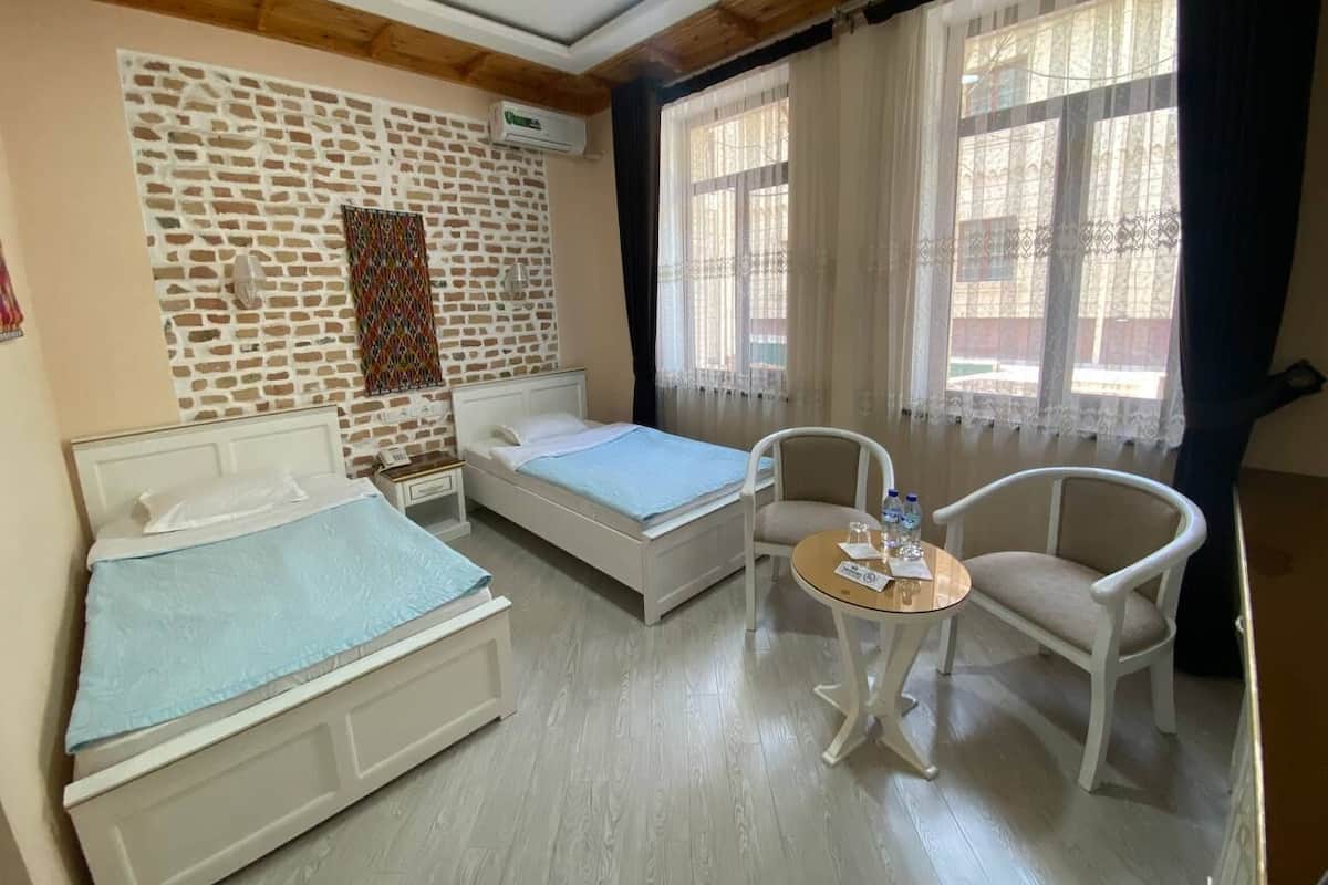 A hotel room with two beds, a small round table, and a chair.