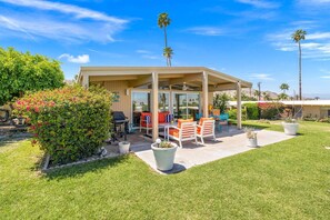 A covered patio with outdoor furniture, a grill, and a view of the surrounding landscape.