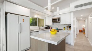 Une cuisine moderne avec des meubles blancs, un îlot central, un four à micro-ondes encastré et une grande fenêtre.