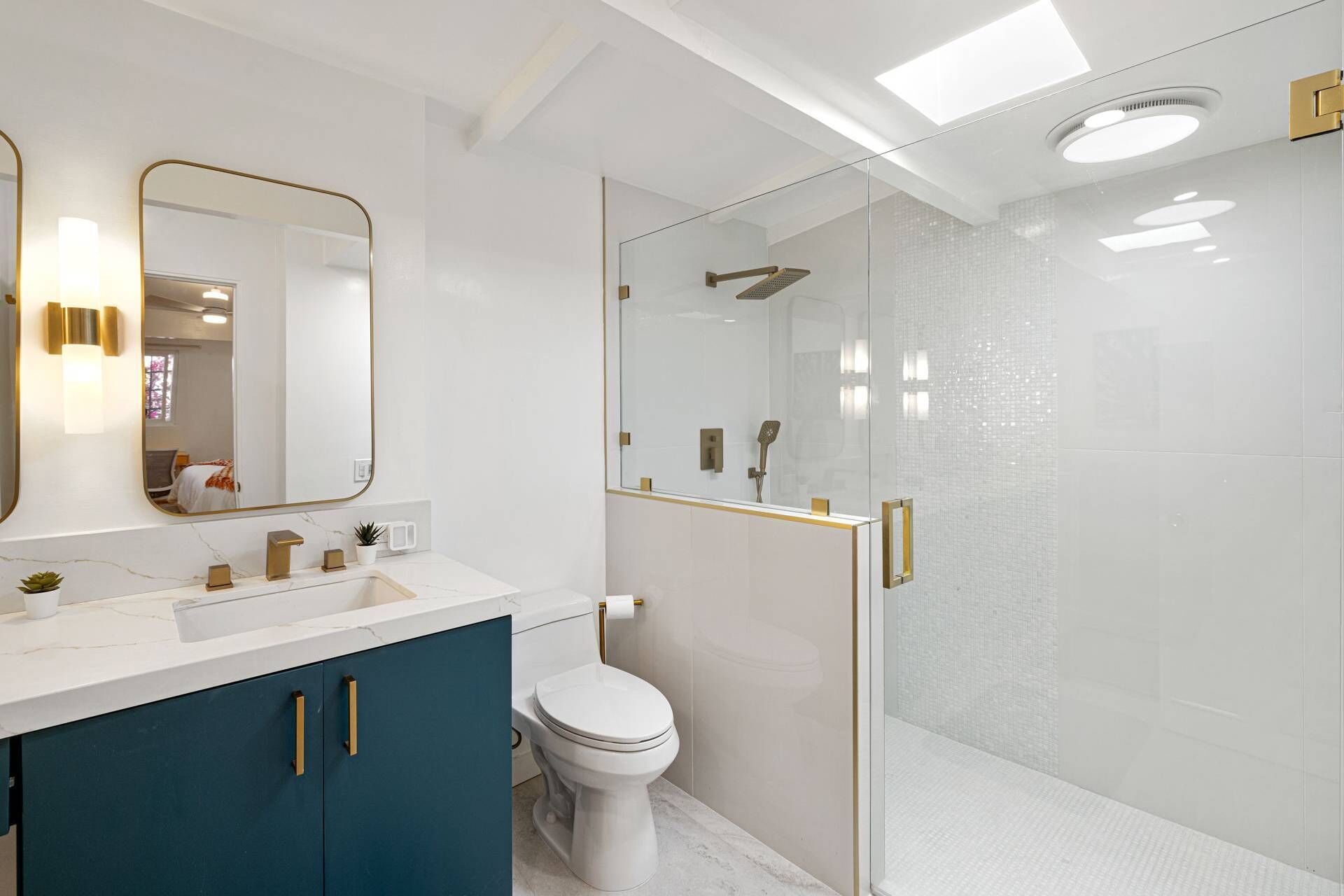 Et moderne badeværelse med et hvidt toilet, en brusekabine med glasvægge og et toiletbord med guldfarvede detaljer.