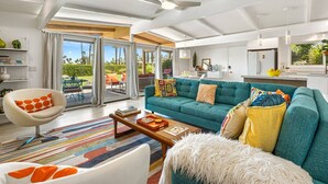 Un salon moderne avec un canapé turquoise, un fauteuil blanc et un tapis rayé aux couleurs vives.