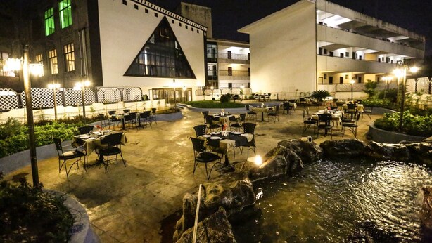Een terras met tafels en stoelen, een waterpartij, en gebouwen met bijzondere architectuur.