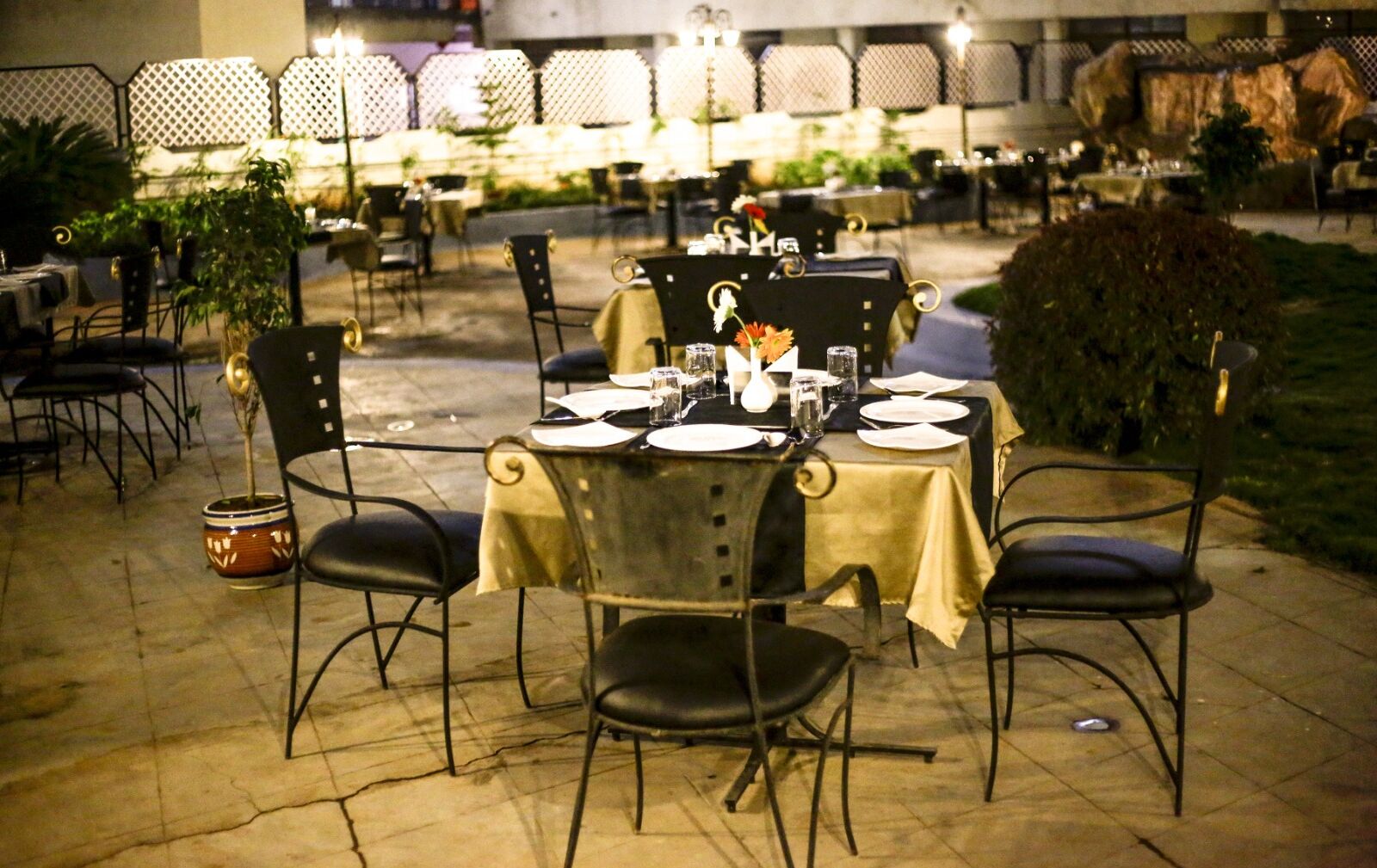 An outdoor dining area with tables set for two, surrounded by chairs.