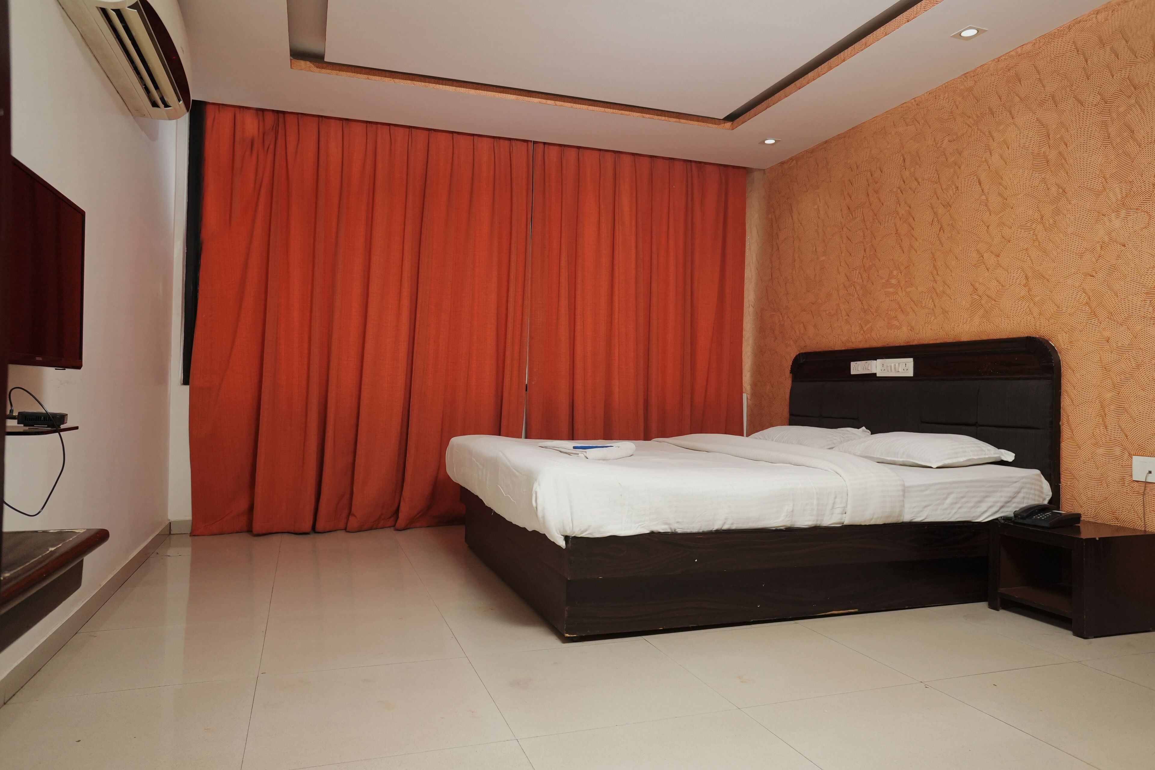 A bedroom with a dark wooden bed, a nightstand, a red curtain, and a wall-mounted air conditioner.