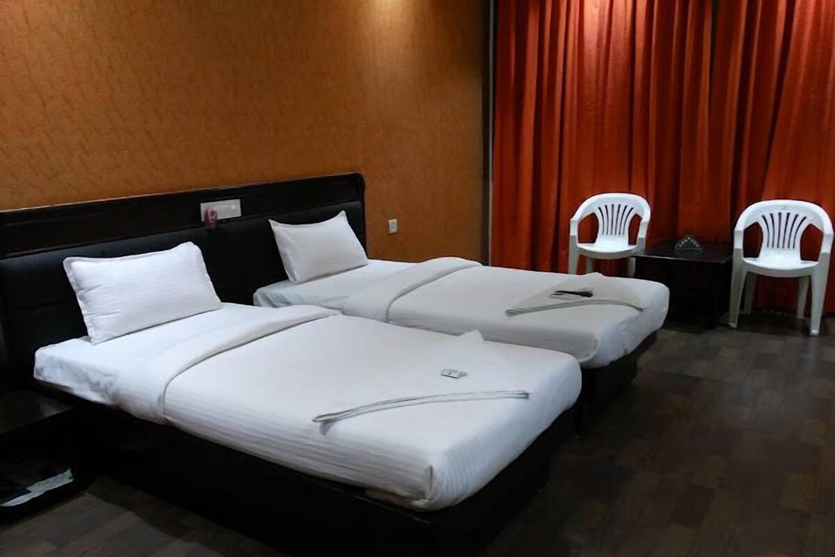 Habitació d'hotel amb dos llits individuals, un capçal de llit de fusta, una cortina vermella i dues cadires de plàstic blanc.