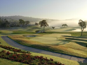 Un parcours de golf avec un chemin bien défini, un drapeau et une étendue d’eau visible au loin.