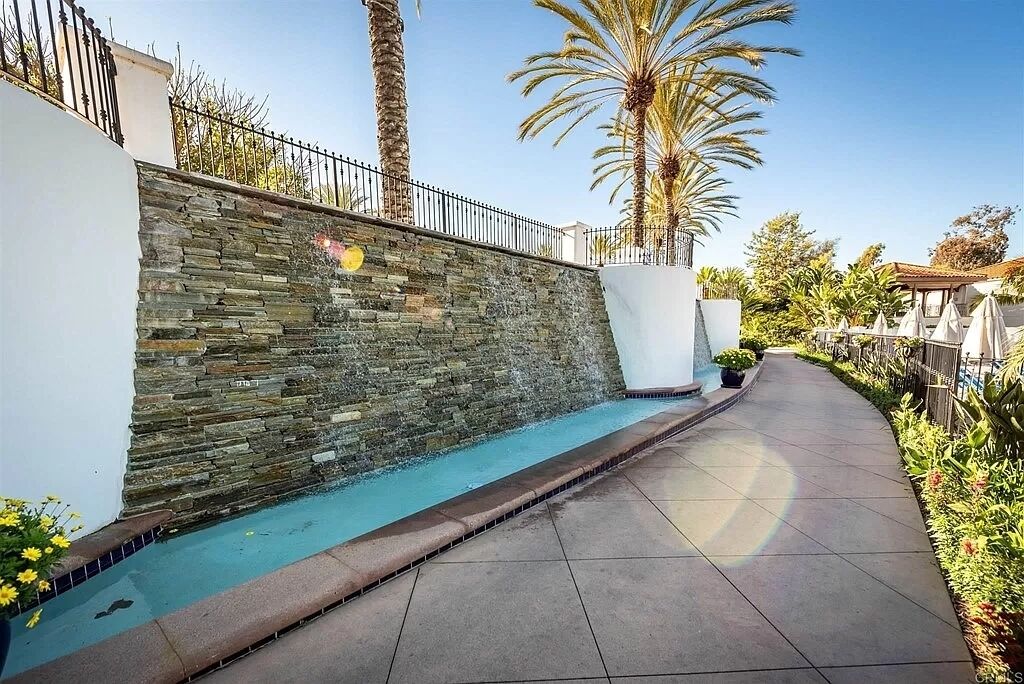 Un mur de pierre, une piscine, un chemin pavé et des palmiers.