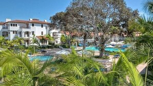 Een resort met een zwembad, palmbomen en witte gebouwen met rode daken.