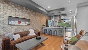 Una sala de estar moderna con pared de ladrillo, un sofá, una mesa de centro y un comedor con taburetes de bar.