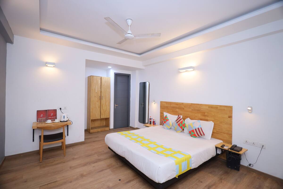 Habitación de hotel con cama, escritorio, silla, armario, ventilador de techo y mesita de noche con teléfono.