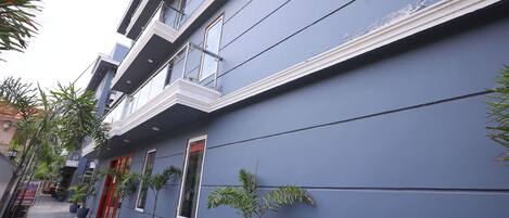 A building with a blue exterior, multiple balconies, and potted plants along the walkway.