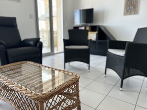 Ein modernes Wohnzimmer mit einem Glastisch, zwei schwarzen Sofas und einem Fernseher auf einem Schrank.