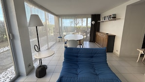 Ein modernes Wohnzimmer mit einem blauen Sofa, einem runden Esstisch und einer Küchenzeile mit Schrank und Regal.