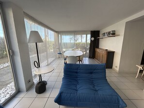 Ein modernes Wohnzimmer mit einem blauen Sofa, einem runden Esstisch und einer Küchenzeile mit Schrank und Regal.