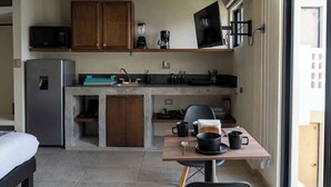 Eine kompakte Küche mit Kühlschrank, Mikrowelle, Kaffeemaschine und einer kleinen Essecke mit Tisch und Stühlen.
