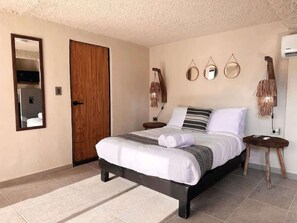 Un dormitorio con cama, una puerta de madera, un espejo y un aire acondicionado instalado en la pared.