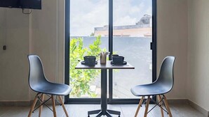 Ein Zimmer mit einer Schiebeglastür, zwei modernen Stühlen, einem kleinen Tisch mit einer Vase und zwei Schalen, sowie einem an der Wand befestigten Flachbildfernseher.