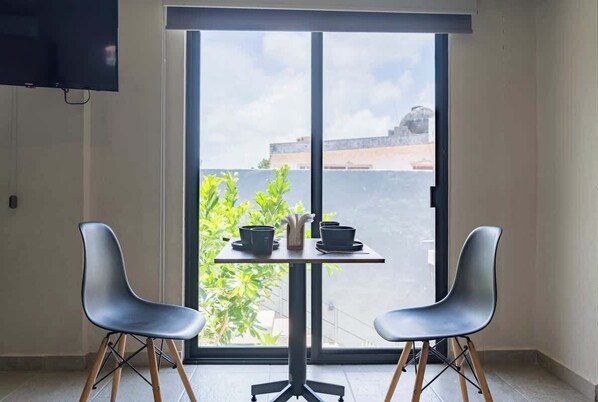 Una habitación con puerta corrediza de vidrio, dos sillas modernas, una mesita con un florero y dos cuencos, y un televisor de pantalla plana montado en la pared.
