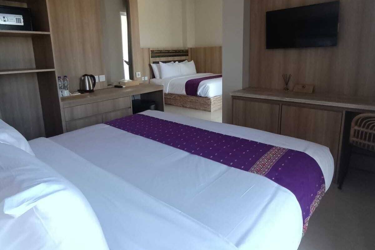 Ein Hotelzimmer mit zwei Betten, einem an der Wand montierten Fernseher und einem Schreibtisch mit Wasserkocher.