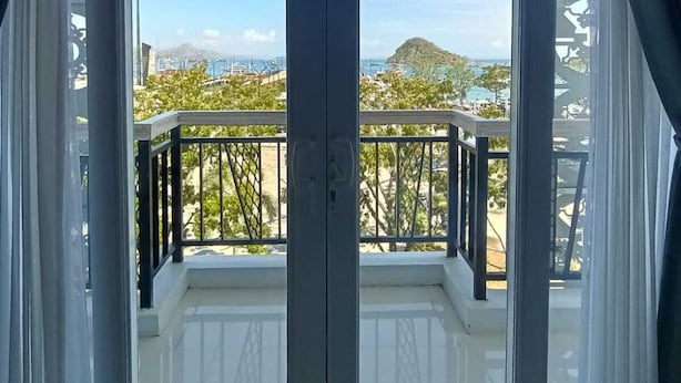 Una gran puerta corrediza de vidrio da a un balcón con vistas a la costa, incluyendo edificios y vegetación.