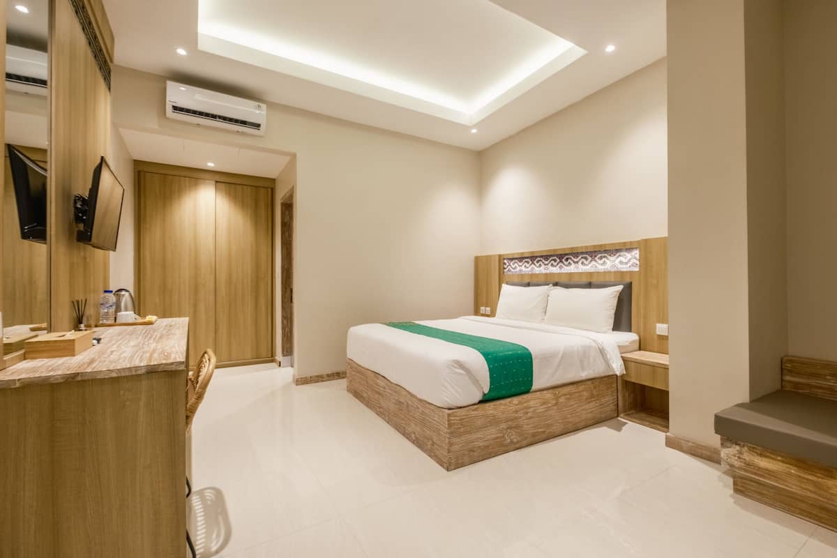 Ein modernes Hotelzimmer mit einem Holzbett, einem kleinen Nachttisch, einer eingebauten Bank, einem Flachbildfernseher und einer Deckenleuchte.