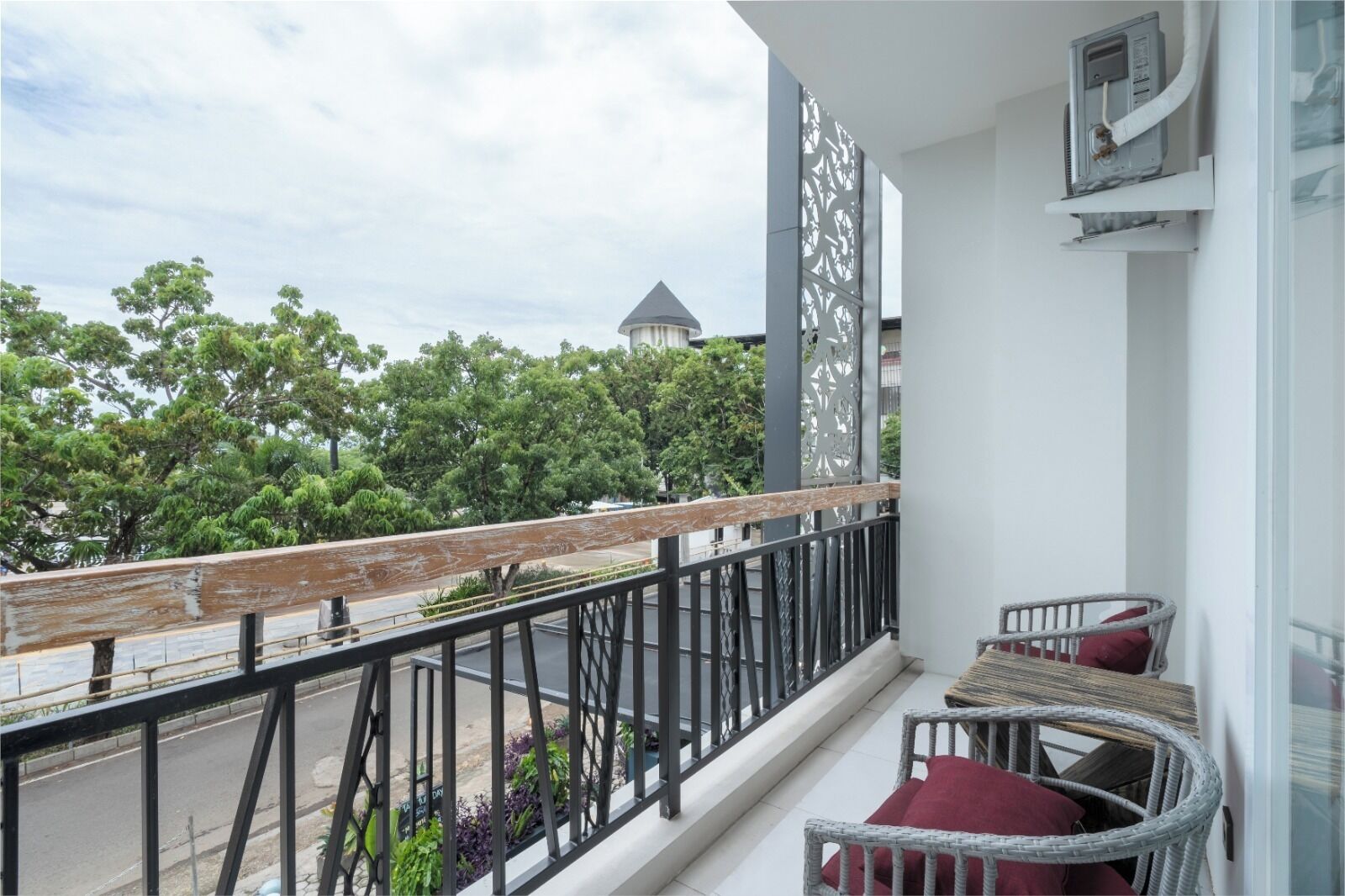 Ein Balkon mit Blick auf Bäume und ein Gebäude, Korbstühle mit Kissen sowie eine weiße Wand mit einer dekorativen Verkleidung.
