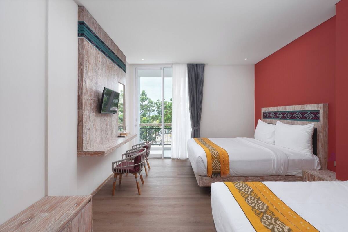 Ein Hotelzimmer mit Bett, Wandfernseher, Balkon mit Tisch und Stühlen sowie einer roten Akzentwand.