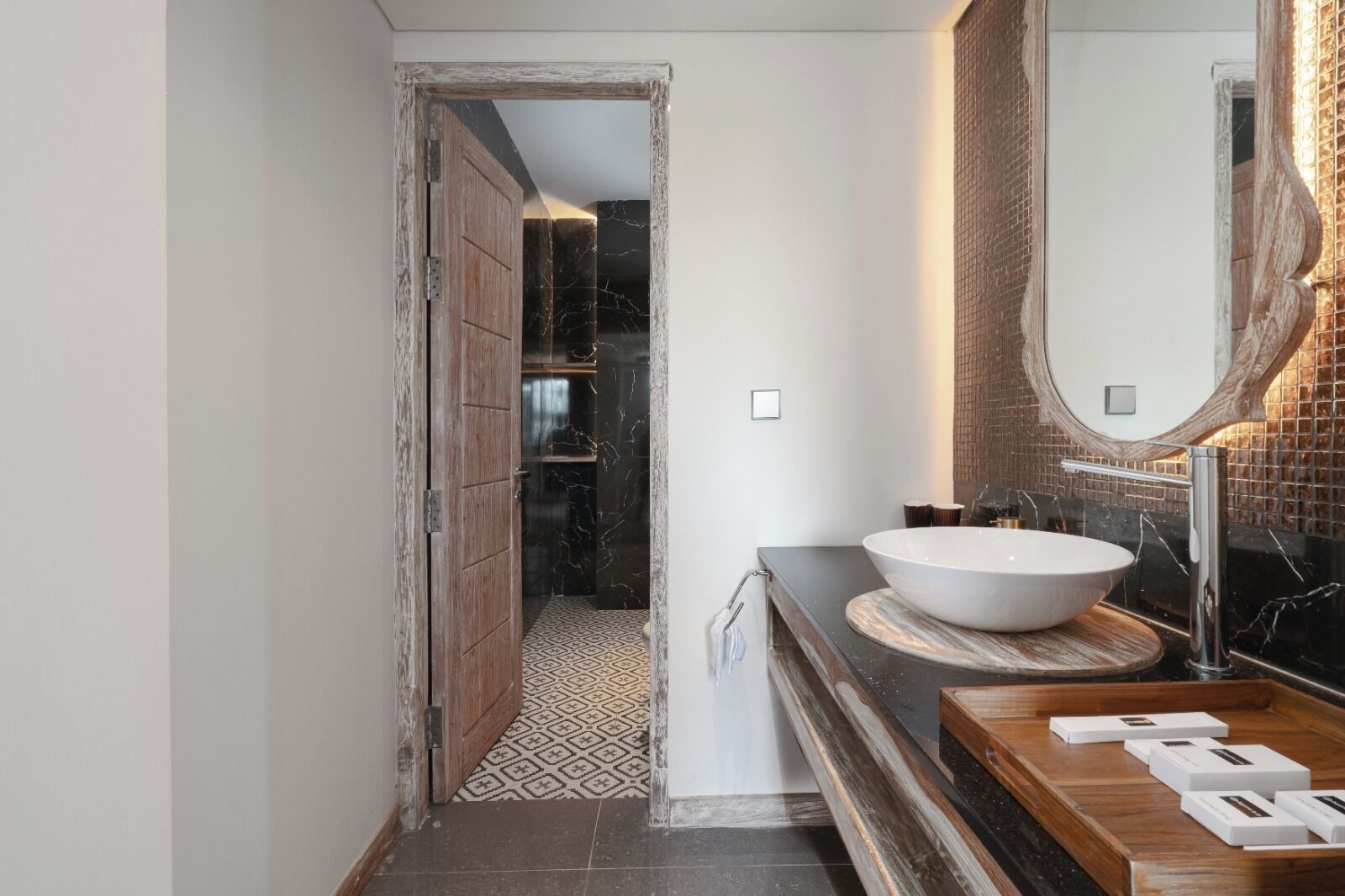 A bathroom with a large white basin, a wooden vanity, and a mirror with a textured frame.