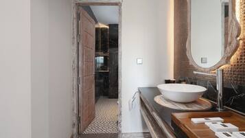 A bathroom with a large white basin, a wooden vanity, and a mirror with a textured frame.