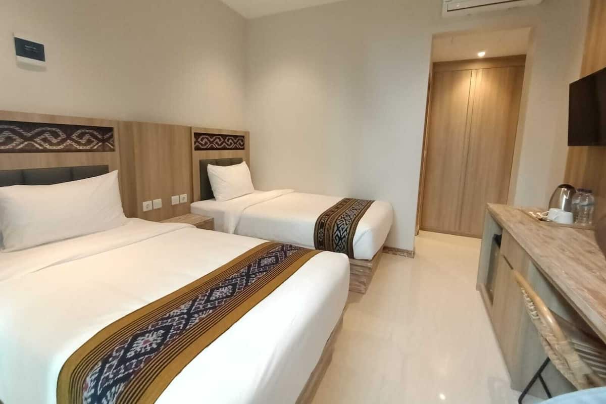 Ein Hotelzimmer mit zwei Betten, einem hölzernen Kopfteil, einem kleinen Nachttisch, einem integrierten Fernseher und einem Kleiderschrank.