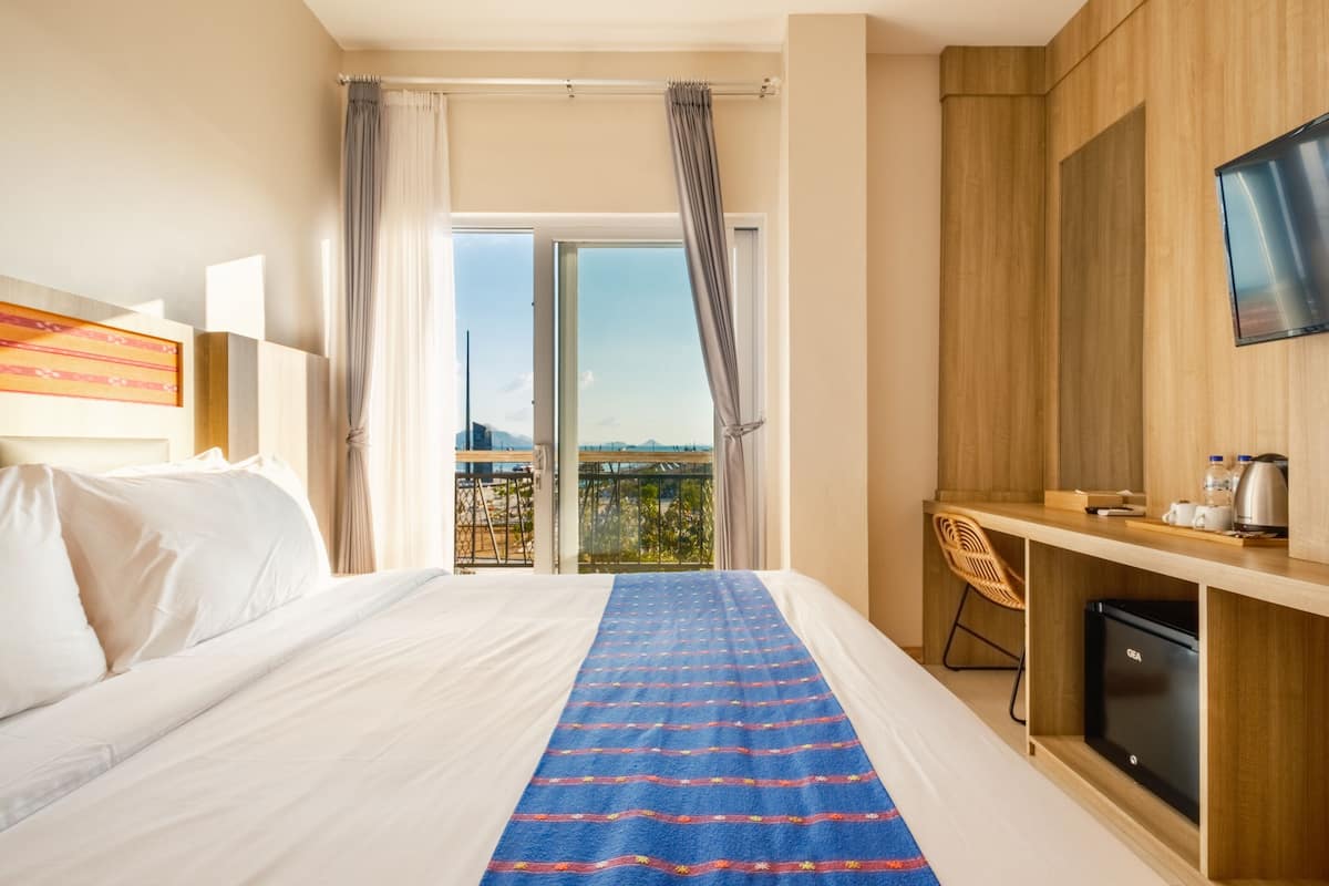 Ein Hotelzimmer mit Bett, Schreibtisch, Sessel, Fernseher und einem Balkon mit Blick.