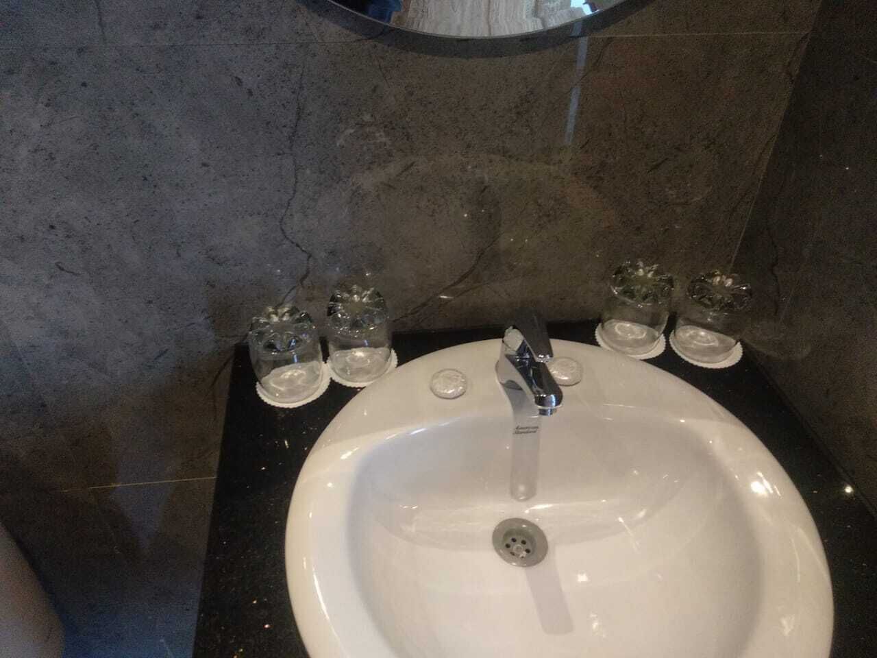 A white sink with a modern faucet, four small glasses on the countertop, and a mirror above the sink.